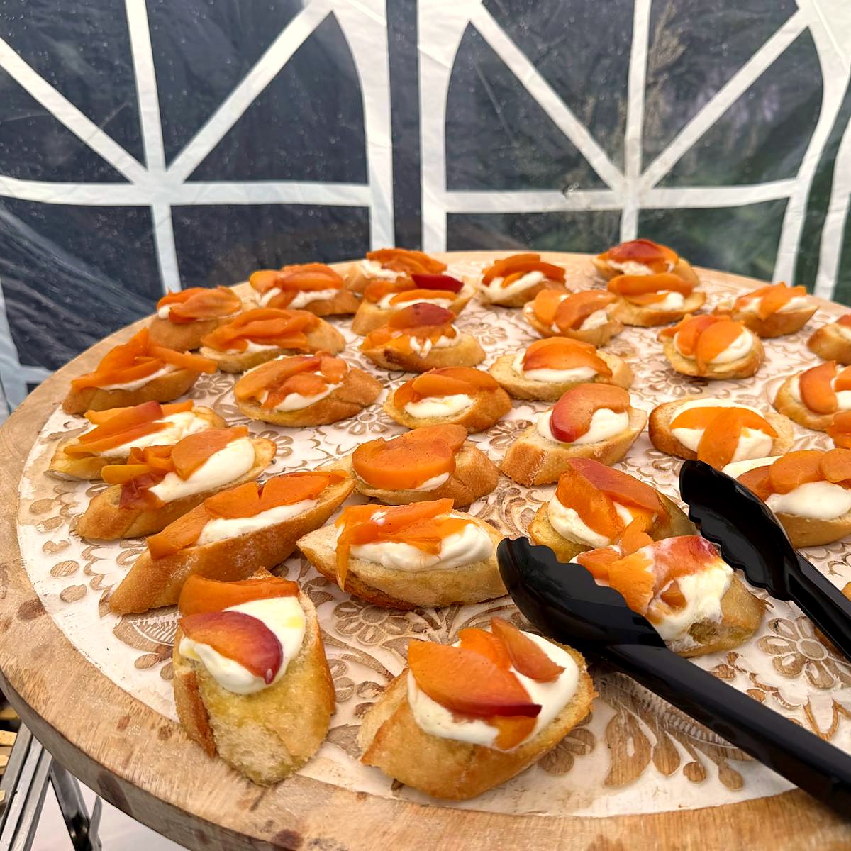 Crostini topped with soft cheese, sliced peach and honey on a carved wooden board
